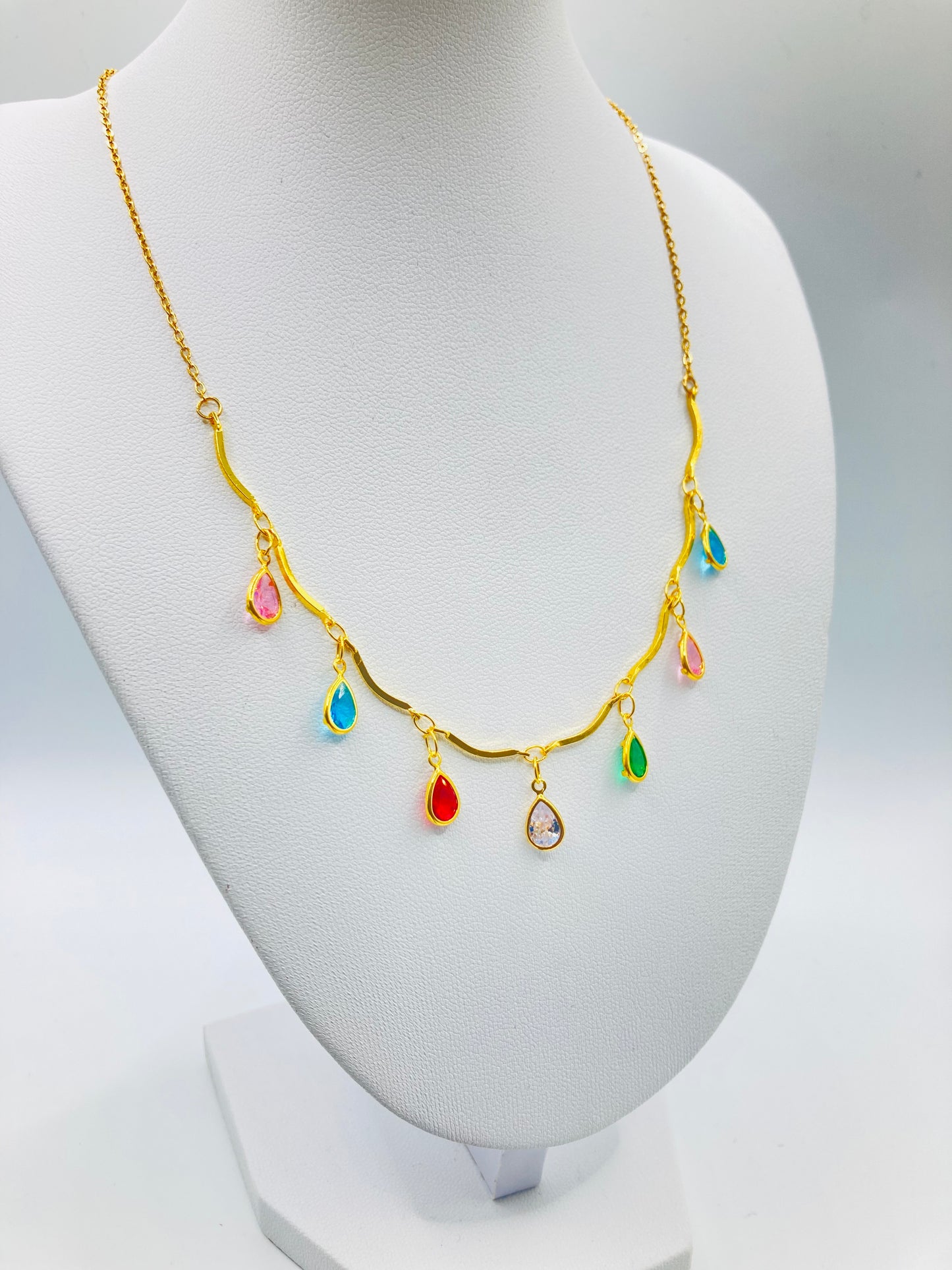 Gold necklace with colorful teardrop-shaped pendants on a mannequin bust.